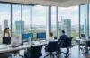 Ein sonnendurchflutetes, modernes Büro mit internationalem Team aus IT-Expertinnen und Experten, die konzentriert an Laptops arbeiten und lebhaft im Austausch sind, umgeben von großflächigen Fenstern mit Blick auf urbane Skylines der EU und USA – ein Bild voller Optimismus, technologischer Innovation und grenzüberschreitender Zusammenarbeit.