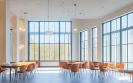 In einem modern gestalteten, hell erleuchteten Konferenzraum tauschen interdisziplinäre Teammitglieder lächelnd Ideen aus, während natürliches Tageslicht warm durch große Fenster fällt und ein Gefühl von gemeinsamer Produktentdeckung, Innovation und motivierender Zusammenarbeit vermittelt.