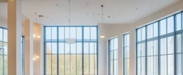 In einem modern gestalteten, hell erleuchteten Konferenzraum tauschen interdisziplinäre Teammitglieder lächelnd Ideen aus, während natürliches Tageslicht warm durch große Fenster fällt und ein Gefühl von gemeinsamer Produktentdeckung, Innovation und motivierender Zusammenarbeit vermittelt.