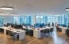 Ein lichtdurchflutetes, modernes Büro mit einem entspannten Team erfahrener Entwickler und Juristen, die konzentriert an Bildschirmen mit KI-Daten und Gesetzesdokumenten arbeiten, dabei warme Holztöne und natürliche Sonnenstrahlen eine freundliche, vertrauensvolle Atmosphäre schaffen.