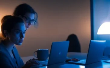 In einem hell erleuchteten, modernen Bürogebäude steht eine nachdenkliche Frau mittleren Alters vor großen Fenstern, während sie vertraut auf einen Laptop blickt, umgeben von warmem Tageslicht und integrierten Pflanzen, die eine Atmosphäre von Vertrauen, Transparenz und verantwortungsvoller digitaler Verwaltung ausstrahlt.