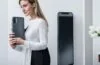 Eine einladende, helle Szene mit einer Person, die entspannt modern wirkende Smartphones in der Hand hält, umgeben von warmem Tageslicht an einem minimalistischen Holzschreibtisch, während im Hintergrund verschwommen helle Fenster und dezente Pflanzen eine freundliche, vertrauensvolle Atmosphäre für digitale Kommunikation und Datenschutz schaffen.