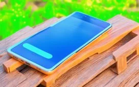 Ein helle, sonnendurchflutete Nahaufnahme eines modernen Smartphones auf einem Holztisch, umgeben von entspannt lächelnden Menschen in heller Kleidung, die gemeinsam konzentriert ihre Geräte sichern – ein warmes, freundliches Setting voller natürlicher Lichtreflexe, das Vertrauen und digitale Sicherheit harmonisch vermittelt.