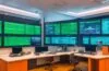 In einem hell erleuchteten, modernen Büro sitzt eine lächelnde IT-Expertin entspannt vor zwei großen Bildschirmen mit offenem NGINX-Dashboard und Zertifikatsverwaltungs-Tools; das natürliche Sonnenlicht durchflutet den Raum, während warme Holztöne und Pflanzen für eine freundliche, einladende Atmosphäre sorgen und die Sicherheit und Automatisierung digitaler Infrastruktur symbolisieren.