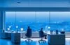 In einem modernen, hell erleuchteten Büro sitzt ein IT-Experte entspannt vor mehreren Bildschirmen, die dynamische Systemanalysen zeigen, während warmes Tageslicht durch große Fenster fällt und eine Atmosphäre von Fortschritt, Innovation und nachhaltiger Technik vermittelt.