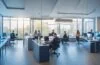 Ein lichtdurchflutetes, modernes Büro mit einem konzentrierten IT-Team, das mit freundlicher Mimik an Laptops und Bildschirmen arbeitet, während warme Sonnenstrahlen durch große Fenster fallen und so eine Atmosphäre von Zuversicht, Zusammenarbeit und digitaler Sicherheit schaffen.