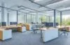 Ein sonnendurchflutetes, modernes Büro mit motivierten IT-Fachkräften in lebendiger Zusammenarbeit an Bildschirmen, die kühle Technik mit menschlicher Wärme verbinden und Vertrauen in die unterstützende Rolle der Künstlichen Intelligenz ausstrahlen.