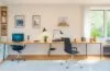 Helle, freundliche Aufnahme eines modernen Home-Office-Arbeitsplatzes mit einem entspannten jungen Menschen, der lächelnd auf ein Smartphone blickt, während natürliches Tageslicht warme Akzente auf minimalistisches Design und digitale Geräte wirft – ein Symbol für die lebensnahe Verbindung von Mensch und sicherer, zukunftsweisender Technologie im digitalen Zeitalter.