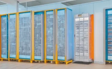 Eine dynamische Szene in einem modern ausgestatteten Rechenzentrum: Eine selbstbewusste Frau mittleren Alters steht lächelnd zwischen leuchtenden Serverracks, während das warme Tageslicht sanft durch große Fenster fällt und ihre engagierte Präsenz als unsichtbare Schlüsselkraft der digitalen Zukunft strahlt.