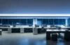 Ein hell erleuchtetes modernes Büro mit konzentriert lächelnden IT-Sicherheitsexperten vor mehreren Bildschirmen, die in natürlichem Tageslicht arbeiten und eine Atmosphäre von Vertrauen, Wachsamkeit und Gemeinschaft schaffen.