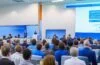 Ein heller, inspirierender Konferenzraum mit modernen, transparenten Bildschirmen, auf denen schemenhafte, digitale Avatare von Wissenschaftlern in lebhaftem Austausch stehen, umgeben von natürlichem Tageslicht, das die freundliche und zukunftsweisende Atmosphäre eines virtuellen KI-Gipfels warm und realistisch einfängt.