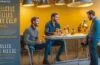 Helles, cineastisch beleuchtetes Großraumbüro mit jungen, vielfältigen Mitarbeitenden in angeregter Diskussion, einladend und warm durch sanftes Tageslicht durchflutet, das eine Atmosphäre von Kreativität und Aufbruch vermittelt.