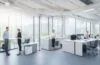 Ein lichtdurchflutetes, modernes Büro mit entspannt arbeitenden Designerinnen und Designern, die an hellen Bildschirmen interaktive Layouts und klar strukturierte Interface-Entwürfe entwickeln, umgeben von warmen Holzakzenten, grünen Pflanzen und natürlichem Tageslicht, das eine einladende Atmosphäre zwischen Kreativität und fokussiertem Teamwork schafft.