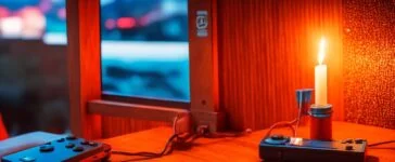 Ein warm beleuchtetes, scharf fokussiertes Foto einer modernen Nintendo Switch 2, die auf einem hellen Holztisch liegt, umgeben von lächelnden Menschen verschiedener Generationen, die entspannt gemeinsam spielen und die neue Hybridkonsole in natürlichem Tageslicht genießen.