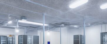 Ein warm ausgeleuchteter, moderner Serverraum mit klar strukturierten Elektroinstallationen und leuchtenden Kontrolllampen, in dem technisches Fachpersonal aufmerksam und konzentriert die Sicherheitsstandards der VDE-Normen überprüft, eingebettet in eine harmonische Atmosphäre aus natürlichem Tageslicht und funktionaler Eleganz.