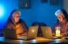 Eine hell beleuchtete, freundliche Büroszene mit einer konzentrierten Frau mittleren Alters, die am Laptop sitzt und aufmerksam eine E-Mail prüft, umgeben von natürlichen Lichtquellen und authentischen Details, die Spannung und zugleich eine warme Vorsicht widerspiegeln.