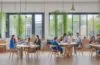Eine helle, warme Aufnahme eines modernen Coworking-Spaces mit einer multikulturellen Gruppe von Menschen, die entspannt und konzentriert an Laptops zusammenarbeiten, während sanftes Tageslicht durch große Fenster fällt und eine Atmosphäre von innovativem Miteinander und digitaler Vernetzung schafft.