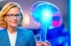 Eine strahlende Büroszene mit einer offenen, freundlichen albanischen Ministerin in moderner Arbeitsumgebung, die konzentriert neben einem digitalen Hologramm oder einem transparenten Bildschirm mit komplexen Daten und KI-Symbolen interagiert, natürliches Tageslicht flutet den Raum und schafft eine warme, einladende Atmosphäre voller Hoffnung und Fortschritt.