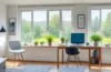 Ein sonnendurchflutetes, modernes Home-Office mit einer fokussierten Person mittleren Alters, die entspannt am Laptop arbeitet, während sanftes Tageslicht durch große Fenster fällt und warme Holztöne dem Raum eine einladende Atmosphäre der digitalen Sicherheit und Achtsamkeit verleihen.