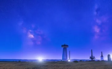 Strahlendes, natürlich beleuchtetes Foto einer modernen Bodenstation mit DE-CIX-Ingenieuren bei der Arbeit, im Hintergrund klar sichtbare LEO-Satelliten am blauen Himmel und sanfte Sonnenstrahlen, die Wärme und die zukunftsweisende Partnerschaft zwischen Netzwerk- und Raumfahrttechnologie einladend vermitteln.