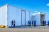 Ein modernes Entwicklerteam arbeitet konzentriert und mit freundlichen Gesten an hell beleuchteten Arbeitsplätzen, umgeben von minimalistischer Technik und transparenten Bildschirmen, die komplexe Container- und Sicherheitsprozesse darstellen, während warme Tageslichtstrahlen durch große Fenster fallen und eine Atmosphäre von Klarheit und Zuversicht schaffen.