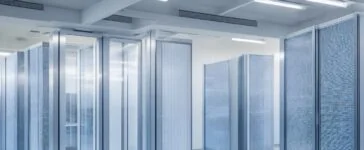 In einem modernen Rechenzentrum strahlt warmes Tageslicht durch große Fenster, während technikaffine Fachleute konzentriert an hochmodernen Serverracks arbeiten und so den lebendigen Geist von Innovation und nachhaltigem Fortschritt in der digitalen Infrastruktur verkörpern.