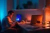 In einem hell erleuchteten, modernen Büro zeigt eine nachdenkliche junge Person mit Laptop und Smartphone in der Hand die spannende Ambivalenz digitaler Überwachung – umgeben von warmem Tageslicht, das die Mischung aus technologischem Fortschritt und menschlicher Verantwortung eindrucksvoll einfängt.