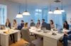 Ein sonnendurchflutetes, modernes Büro mit einem freundlichen Marketing-Team, das konzentriert vor Laptopbildschirmen sitzt, während natürliche Lichtstrahlen warm die Szene erhellen und den innovativen Einsatz von KI-Technologie in der digitalen Kommunikation lebendig widerspiegeln.