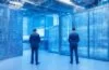 Ein warm erleuchteter, moderner Serverraum mit strahlend weißen Wänden und glänzenden Glasflächen, in dem gut gelaunte Mitarbeitende in legerer Businesskleidung mit offener Kommunikation und natürlichem Tageslicht die digitale Infrastruktur eines hochmodernen Rechenzentrums an einem Tag der offenen Tür vorstellen.