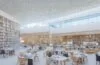 Ein sonnendurchfluteter, moderner Bibliotheksraum in Berlin mit offenen Fenstern, an hellen Holztischen sitzen lachende Menschen unterschiedlichster Altersgruppen, vertieft in digitale Geräte und Bücher, während im Hintergrund hohe Regale voller Bücher und dezente Glasfaserkabelverbindungen eine Atmosphäre von Innovation, Bildung und gemeinschaftlichem Aufbruch schaffen.