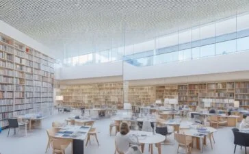 Ein sonnendurchfluteter, moderner Bibliotheksraum in Berlin mit offenen Fenstern, an hellen Holztischen sitzen lachende Menschen unterschiedlichster Altersgruppen, vertieft in digitale Geräte und Bücher, während im Hintergrund hohe Regale voller Bücher und dezente Glasfaserkabelverbindungen eine Atmosphäre von Innovation, Bildung und gemeinschaftlichem Aufbruch schaffen.