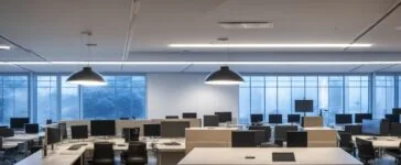 Ein hell erleuchtetes, modernes Büro mit warmem Tageslicht, in dem eine diverse Gruppe von Fachleuten konzentriert und doch entspannt an Laptops und Tablets arbeitet, während im Hintergrund eine große Tafel mit komplexen Daten und Diagrammen eine Atmosphäre intensiver Forschung und technischer Innovation vermittelt.