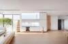Ein sonnendurchfluteter, minimalistischer Wohnraum im japanischen Stil, der harmonisch smarte Technologie und klares Design vereint, mit warmen Holztönen, dezent integrierten digitalen Steuerflächen und einer einladenden Atmosphäre voller Ruhe und Funktionalität.