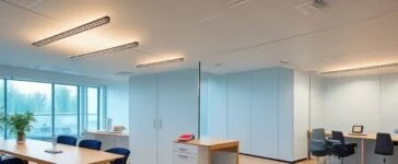 Ein warm beleuchtetes, modernes Büro mit klaren Linien und natürlichem Tageslicht, in dem ein konzentrierter Mann mittleren Alters – repräsentativ für einen Technologie-CEO – entspannt vor mehreren Bildschirmen mit digitalen Diagrammen und KI-Datenmodellen sitzt, während im Hintergrund ein großes Fenster eine sonnige Skyline mit urbaner Dynamik zeigt, die den Wandel und die Herausforderung in der KI-Ära symbolisiert.