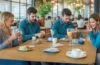Eine helle, warme Aufnahme eines entspannten jungen Erwachsenen in modernem Café, der mit einem freundlichen Lächeln sein Smartphone sicher und komfortabel kontaktlos an ein stilvolles Bezahlterminal hält, während sanftes Tageslicht durch große Fenster fällt und die Szene eine einladende, vertrauensvolle Atmosphäre ausstrahlt.
