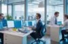 Ein lebendiges, editorial wirkendes Foto in warmem Tageslicht, das einen modernen Softwareentwickler in einem hellen, freundlichen Büro zeigt, der konzentriert vor mehreren Bildschirmen mit komplexen Programmier- und KI-Daten arbeitet, während im Hintergrund eine große Fensterfront weiches Sonnenlicht hereinflutet und eine Atmosphäre von Innovation, technischer Herausforderung und optimistischer Arbeitsplatzdynamik schafft.