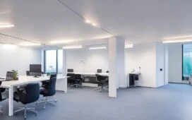 Ein hell erleuchtetes, modernes Büro mit entspannten Kreativen verschiedener Generationen, die bei natürlichem Tageslicht lebhaft über Kunstwerke und digitale Bildschirme diskutieren – symbolisch für den lebendigen Dialog zwischen menschlicher Kreativität und KI im Spannungsfeld von Innovation und Urheberrecht.