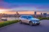 Ein strahlender Mercedes-Benz GLC parkt vor einem sonnenbeschienenen, modernen Stadtpanorama, das durch warmes, natürliches Licht beleuchtet wird und die klassischen, eleganten Linien des SUV mit seiner markanten Front und vertrauten Silhouette emotional und einladend in Szene setzt.