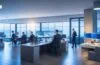 In einem hell erleuchteten, modernen Büro sitzt ein nachdenklich lächelnder Mann mittleren Alters in legerer Businesskleidung vor einem großen Bildschirm voller Daten und schematischer KI-Grafiken, während warmes Tageslicht durch große Fenster fällt und eine Atmosphäre von fokussierter Zuversicht und aufkeimender Innovation schafft.