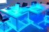 In einem modernen, hell erleuchteten Büro sitzen mehrere junge Fachkräfte entspannt um einen großen Tisch, während ein digital animiertes Hologramm eines abstrakten Chatbot-Symbols über einem Laptop schwebt und lebendig Informationen austauscht – die warme Tageslichtatmosphäre unterstreicht die innovative Verbindung von künstlicher Intelligenz und internem Unternehmenswissen.