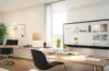 Ein lichtdurchflutetes, modernes Büro mit einem fokussierten Webdesigner, der vor mehreren großformatigen Bildschirmen voller klar strukturierter, responsiver Webseiten arbeitet, umgeben von warmen Holzmöbeln und sanftem Tageslicht, das eine Atmosphäre von Innovation, Präzision und technischer Meisterschaft schafft.