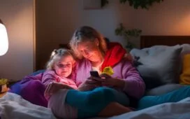 Ein warmes, natürlich beleuchtetes Portrait einer sorgenden Mutter und ihres Kindes, die gemeinsam auf ein Smartphone schauen, während sie in einem hellen, gemütlichen Wohnzimmer sitzen – die Atmosphäre strahlt Vertrauen, Nähe und den achtsamen Umgang mit digitaler Mediennutzung aus.