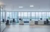 In einem hell erleuchteten, modernen Büro stehen engagierte Expert:innen in angeregtem Austausch vor modernen Bildschirmen, während warme Sonnenstrahlen durch große Fenster fallen und eine Atmosphäre von Innovation, Fokus und neuer Aufbruchsstimmung schaffen.