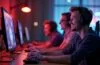 Ein strahlend helles, atmosphärisch warmes Studio mit moderner Gaming-Hardware, in dem eine diverse Gruppe konzentrierter Entwickler um einen leuchtenden Bildschirm versammelt ist, während weiches Tageslicht ihre begeisterten Gesichter sanft umspielt – ein Sinnbild für die innovative Verschmelzung von Künstlicher Intelligenz und Spieleentwicklung unter Elon Musks visionärer Führung.