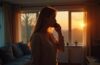 Eine helle, natürlich beleuchtete Szene in einem modernen Wohnzimmer, in der eine besorgte Frau mit aufmerksamer Miene telefoniert, während sanftes Sonnenlicht durch große Fenster fällt und eine warme, vertrauensvolle Atmosphäre schafft, die zugleich die unterschwellige Anspannung vor einem möglichen Betrugsanruf spürbar macht.