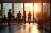 Ein lichtdurchflutetes, modernes Büro mit freundlichen europäischen Fachleuten in angeregtem Austausch vor großen Fenstern, die sanftes Tageslicht hereinlassen und die innovative Atmosphäre einer gemeinsamen Technologie-Zukunft aus Prozessoren und Cloudprojekten warm und lebendig widerspiegeln.