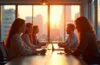 In einem hell erleuchteten, modernen Büro mit großem Panoramafenster tauschen sich diverse, konzentrierte Tech-Expert:innen unterschiedlicher Herkunft lebhaft über Zukunftstechnologien aus, während warme Sonnenstrahlen eine inspirierende Atmosphäre schaffen und innovative Köpfe im Wettlauf um KI-Talente vereinen.