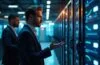Ein helle, warm ausgeleuchtete Aufnahme eines modernen Serverraums mit konzentrierten IT-Profis im Gespräch vor hochauflösenden Bildschirmen und sichtbaren Container-Dashboards, die ein Gefühl von Sicherheit und technischer Präzision ausstrahlt.