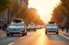 Ein heller, einladender Stadtblick bei Tageslicht zeigt moderne Elektroautos verschiedener Marken entspannt auf breiten Straßen fahren, begleitet von freundlichen Menschen am Gehweg, die neugierig und hoffnungsvoll auf die Zukunft des autonomen Fahrens blicken – eine harmonische Momentaufnahme technologischer Innovation und urbaner Mobilität.