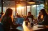 Ein warm erleuchteter, moderner Arbeitsplatz mit Entwickler:innen, die konzentriert an Laptops mit geöffneten Code-Editoren und Git-Tools arbeiten, umgeben von Holz- und Pflanzenakzenten, die eine entspannte, produktive Atmosphäre voller Fokus und Zusammenarbeit ausstrahlen.